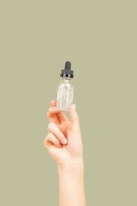 A hand holding a clear glass dropper bottle representing CBD oil tincture